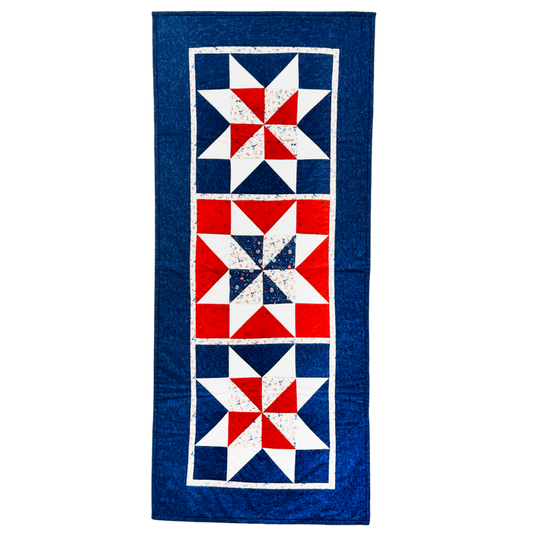 A vintage-style quilt runner featuring three vertical panels with red, white, and blue starburst patterns, finished with a wide blue border.
