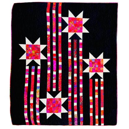 A square quilted textile featuring a black background with four starburst motifs in white and bright pink, red, orange, and purple patterned fabric, connected by vertical striped columns in pink, white, and black.
