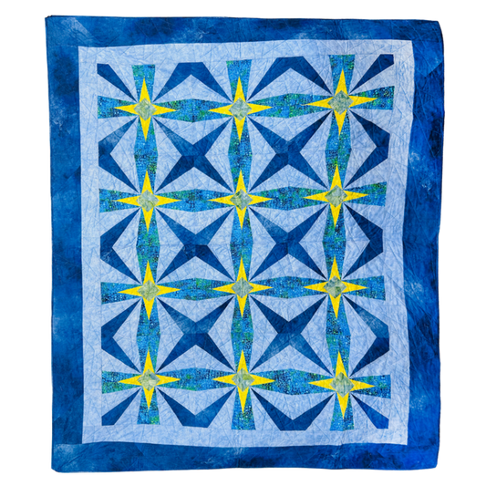 A square quilt with a geometric starburst pattern, featuring shades of blue, navy, and yellow on a white background with a blue border.