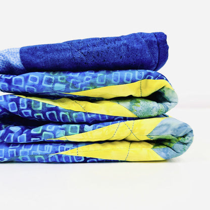 A stack of three folded quilted blankets in blue and yellow patterns, shown on a clean white background.